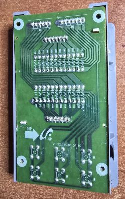 Spód zielonej płytki PCB z lutami i ścieżkami, częściowo w szarej obudowie