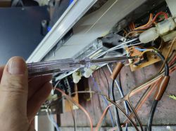 Osoba trzyma próbnik napięcia przy układzie elektronicznym z widocznymi przewodami.