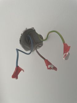 Three electrical wires emerging from the wall: brown, blue, and green/yellow, each with a red insulating cap.