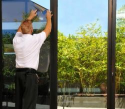 Man applying adhesive film on glass balcony doors with a view of the garden.