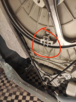 Wnętrze pralki z czerwonym okręgiem wokół elementu w obudowie z tworzywa sztucznego.