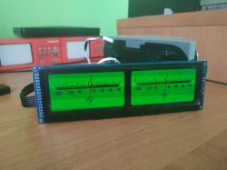 Backlit green LCD module displaying two analog-style VU meters on a desk