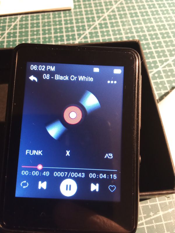 Ekran odtwarzacza muzyki z utworem „08 - Black Or White” i ikoną płyty, na tle maty do cięcia.