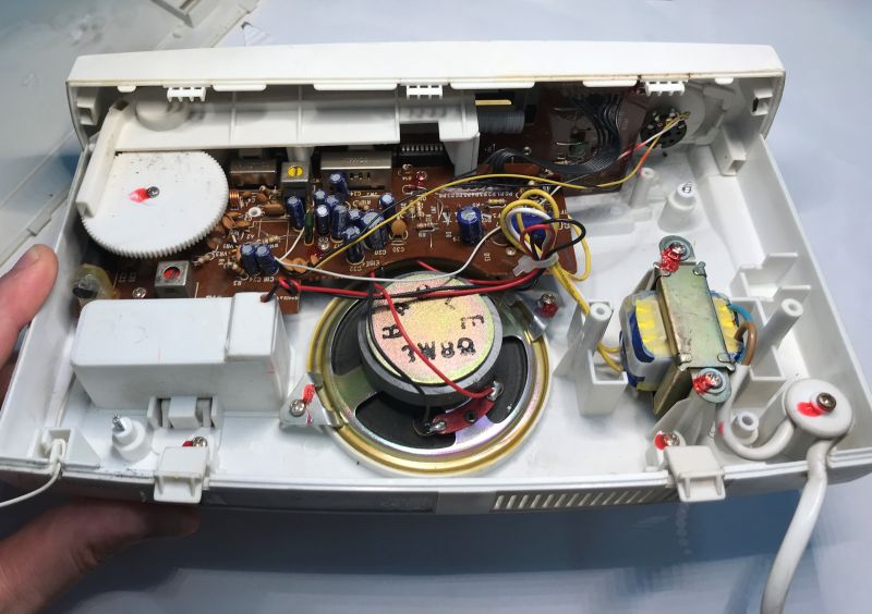 Inside a white radio: PCB, speaker, transformer, and a tuning mechanism with a large gear wheel