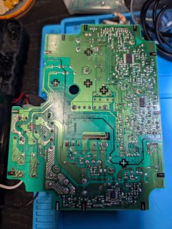 Underside of a green PCB with solder joints and traces on a blue repair mat