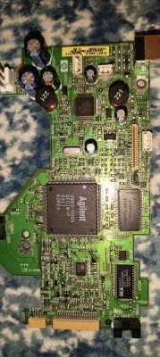Zielona płytka PCB z układami Agilent i pamięcią, kondensatorami oraz złączami, na niebieskim tle
