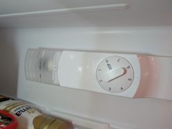 Innenraum eines Kühlschranks mit Lampenabdeckung und Thermostat-Drehknopf.
