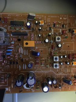 Zbliżenie na fragment płytki drukowanej z elementami elektronicznymi: kondensatorami, rezystorami, układami scalonymi i złączami.