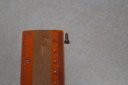 Screw Next to Ruler A small screw lies next to an orange ruler on a light background.