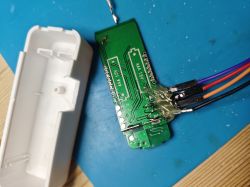 Circuit board with attached wires and white casing on a blue mat.