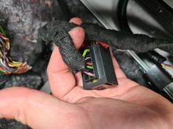 Close-up of a hand holding an electrical connector with colorful wires wrapped in fabric tape.
