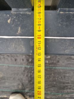 Miarka zwijana przyłożona do stalowego elementu bramy z widoczną odległością około 13 cm.