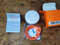 Sonoff SNZB-01P, instrukcja, taśma montażowa i opakowanie na drewnianej powierzchni.