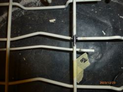 Zardzewiałe miejsce na metalowym koszu zmywarki oznaczone taśmą z numerem 8V.