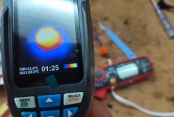 Obrazek przedstawia termometr na podczerwień z wyświetlaczem wskazującym temperaturę 65,0°C.