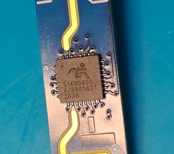S1KM0000 integrated circuit on blue PCB with gold traces and visible QFP pins