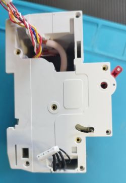 Partially disassembled white electrical module with multicolored and black wires protruding, placed on a blue technical mat.