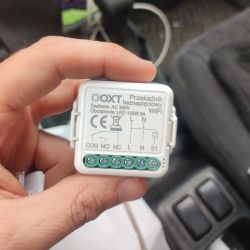 A person holds an OXT WiFi voltage-free relay module with visible labels and connectors.