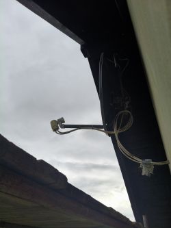 Antena satelitarna zamocowana pod dachem z widocznymi przewodami wychodzącymi z konwertera, z których dwa są luźne.