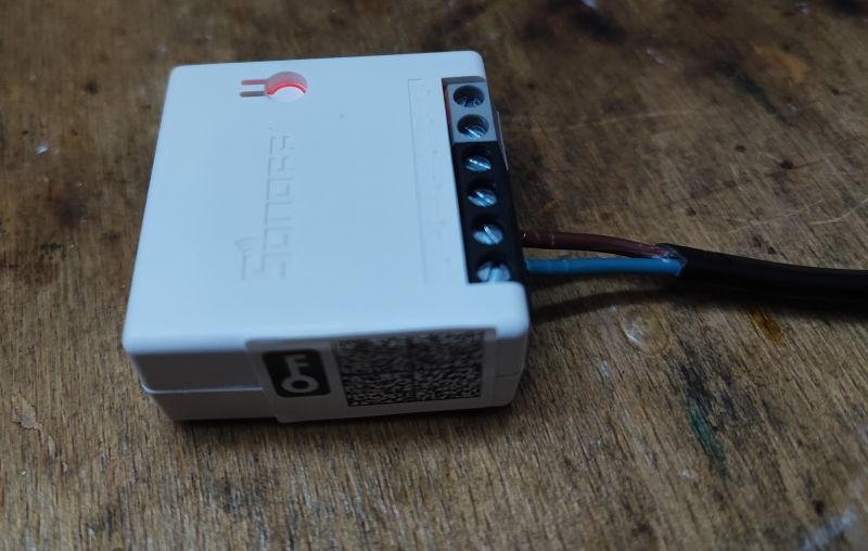 Sonoff ZBMini Zigbee Relay Sonoff ZBMini is a small, white Zigbee relay with wiring, placed on a wooden surface.