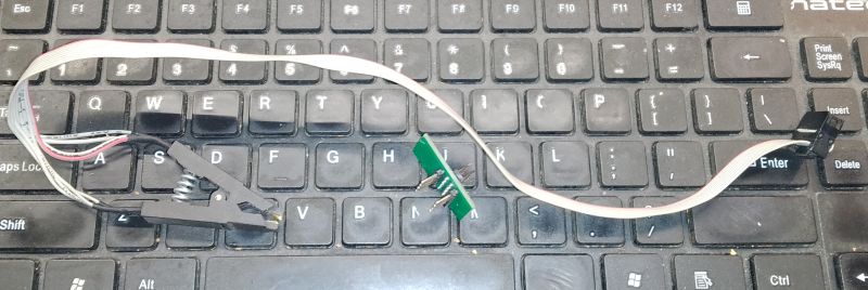 SPI programmer clip connected to adapter, lying on a laptop keyboard