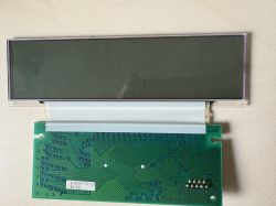 Wyjęty wyświetlacz LCD z płytką PCB i taśmą połączeniową, leżący na jasnej powierzchni.