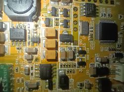 Zbliżenie na płytkę drukowaną PCB z widocznymi kondensatorami tantalowymi, układami scalonymi i innymi elementami elektronicznymi.