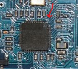 Close-up of a blue PCB with an integrated circuit and a red arrow pointing to one pin.