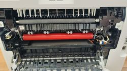 Wnętrze rozebranego urządzenia biurowego z widocznymi elementami mechanicznymi i elektrycznymi.