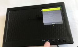 Small black monitor with picture settings menu in the top right, finger pressing a bottom bezel button