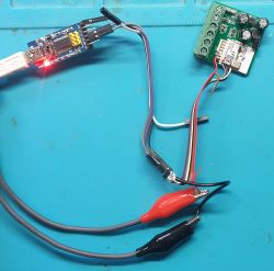 Electronic module connected by wires to USB adapter on a workbench.