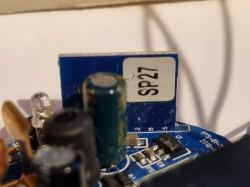 Close-up of a blue PCB with capacitors, an LED and an IC; “SP27” sticker in the background.