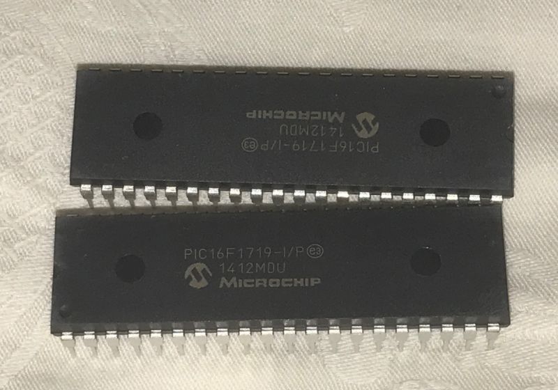 Two Microchip PIC16F1719-I/P Chips Two Microchip chips with logo and designation PIC16F1719-I/P lying on a white background.