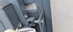 Zbliżenie na zawias bramy montowany na metalowym słupku przy elewacji budynku