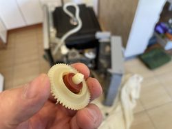Plastikowe zębatka z uszczelką trzymana w dłoni, w tle rozebrane urządzenie domowe.