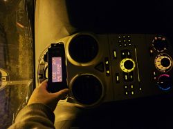 Osoba trzymająca wyświetlacz radia samochodowego przed deską rozdzielczą nocą.