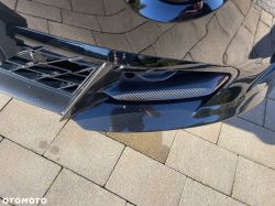 Close-up of a black car front bumper with grille and air intake featuring a carbon-fiber-like trim