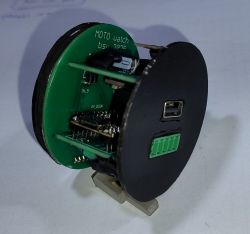 Okrągłe urządzenie elektroniczne z płytkami PCB i portem USB, widok z boku na białym tle