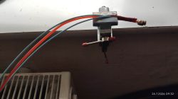 Small metal vise gripping a wire; red and blue cables above a radiator.