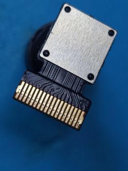 Camera Module with 18-pin FFC/ZIF Connector Camera module with metal shield and 18-pin FFC/ZIF connector, front view on blue background.