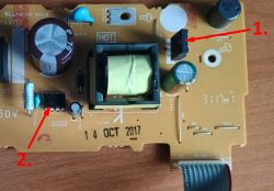 Płytka drukowana z zaznaczonymi dwoma elementami elektronicznymi oznaczonymi cyframi 1 i 2 czerwonymi strzałkami.