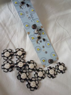 Płytka elektroniczna z elementami LED, leżąca na białym tle, obok innych modułów LED.