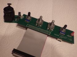 Elektronikplatine mit mehreren Schaltern und einer Buchse, verbunden durch ein Flachbandkabel.