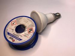 A soldering wire spool with wire next to an LED bulb on a table.