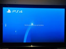 Ekran telewizora z włączonym ekranem startowym PlayStation 4 na niebieskim tle