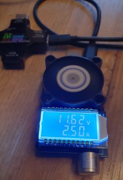 Zbliżenie na elektroniczne obciążenie z wentylatorem i ekranem LCD pokazującym 11,62 V i 2,50 A