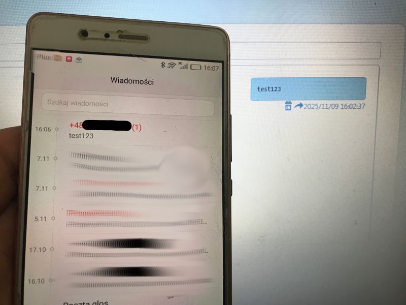 Telefon wyświetlający wiadomość SMS „test123” przed monitorem z tym samym komunikatem