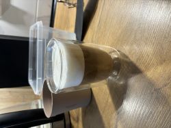 A glass of latte macchiato with thick foam on a wooden table.