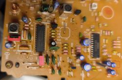 Close-up of a PCB with ICs, capacitors, and resistors; two parts in the lower-right corner outlined in red