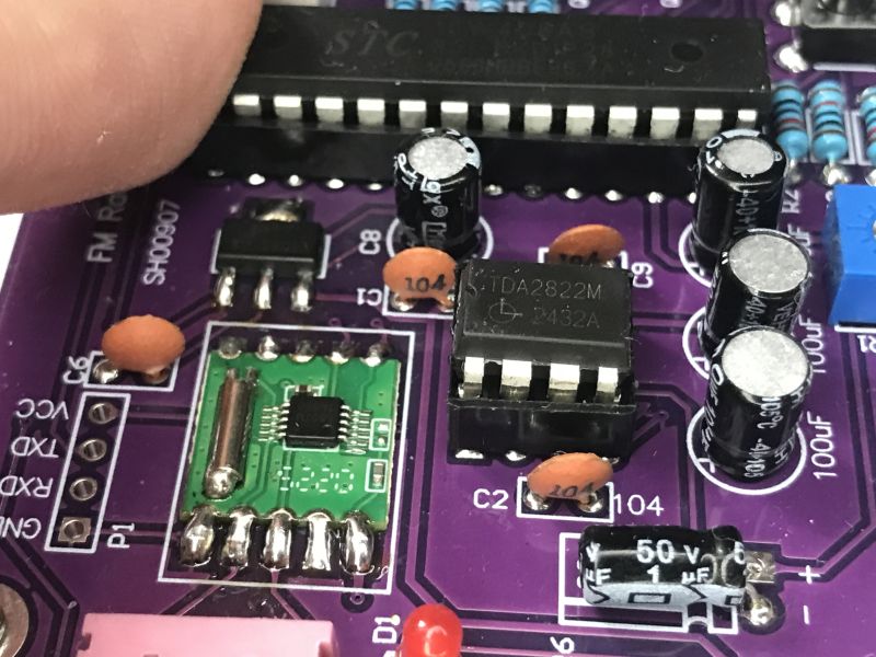 Close-up of a purple PCB with an FM tuner module, TDA2822M IC, and several electrolytic capacitors